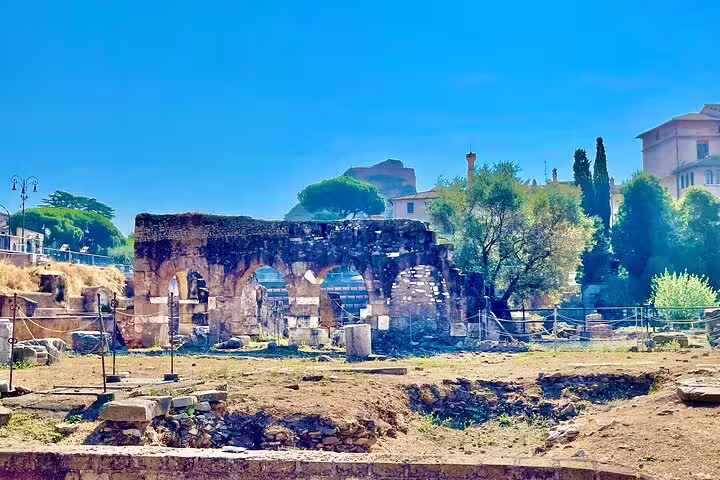 Ancient stone arches and ruins of the Roman Forum under a clear blue sky on a guided Rome Colosseum panoramic tour