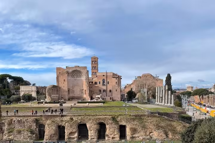 Panoramic view of the Roman Forum ruins under a blue sky, showcasing ancient architecture and columns.