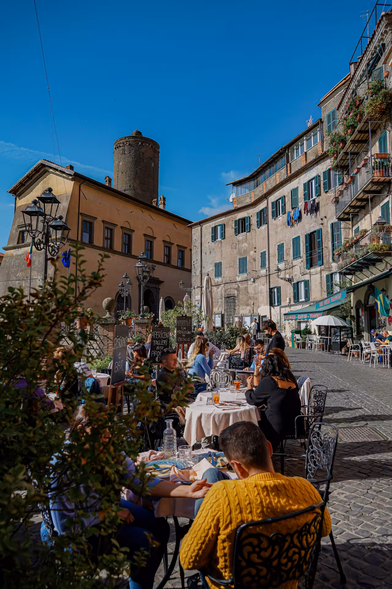 Charming Italian piazza with outdoor dining, ancient tower, and vibrant atmosphere on the Roman Hills Vintage Tour.