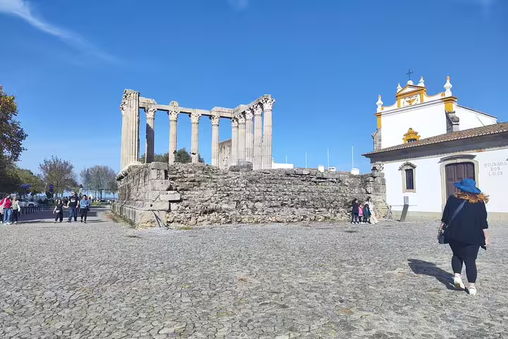 Roman Temple of Évora under a clear blue sky, surrounded by tourists exploring the historic site.