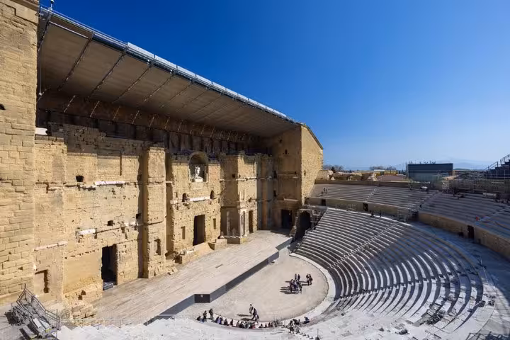 Ancient Roman theatre of Orange with semicircular seating and massive stage wall under clear blue sky