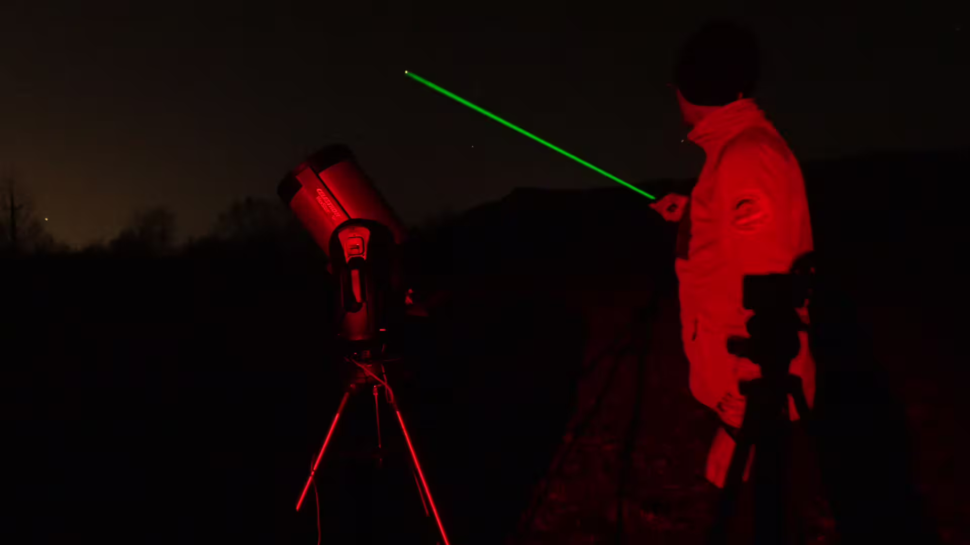 Astronomer pointing green laser pointer at night sky beside telescope during Romania stargazing tour