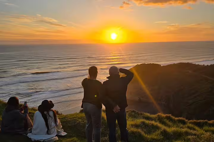 Couples enjoying a breathtaking sunset over Auckland's coastline, ideal for a romantic tour including winery and thermal pool.