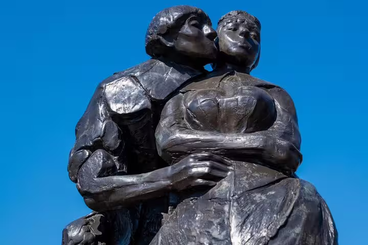 Bronze sculpture of two figures embracing and kissing against a blue sky in Amsterdam