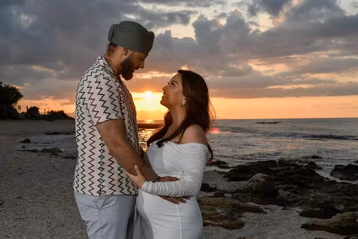 Romantic couple gazing at each other on Ammoudara shore with a stunning sunset backdrop.
