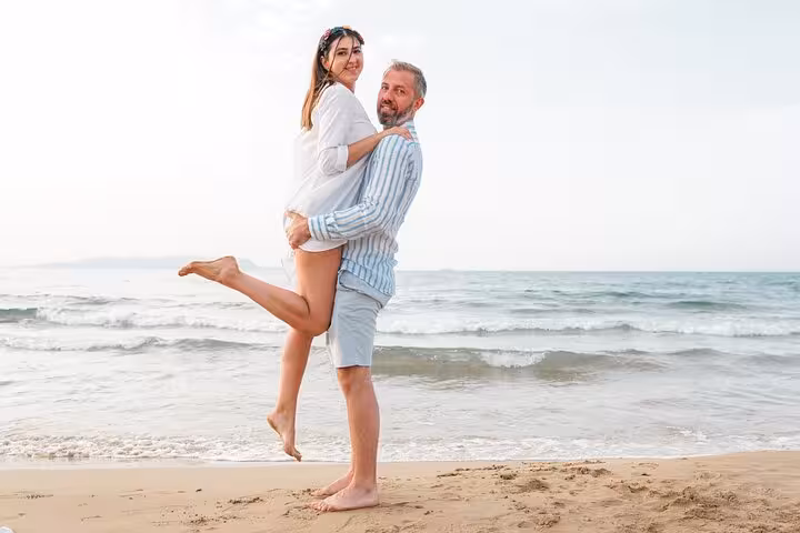 Man playfully lifting woman on a sandy beach during a romantic private photoshoot in Hersonissos, Crete, Greece.