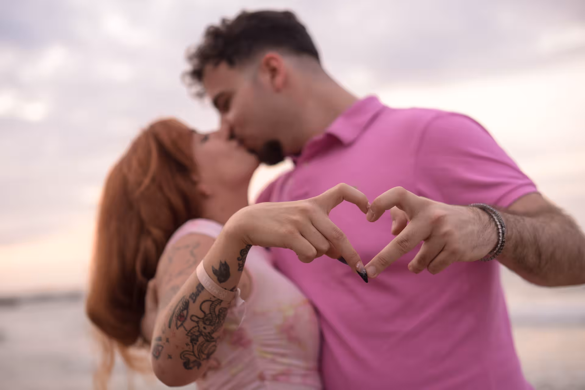 Romantic couple kissing at Heraklion Venetian Port, forming a heart with their hands during a sunset photoshoot.