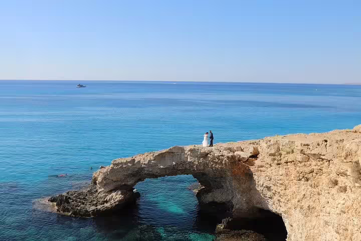 Romantic couple standing on a natural rock arch over turquoise waters during a professional photoshoot in Ayia Napa.