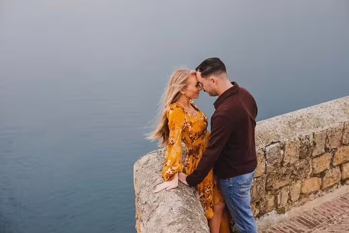 Romantic couple embraces on a scenic stone balcony overlooking the serene sea in Naples, perfect for a photoshoot.