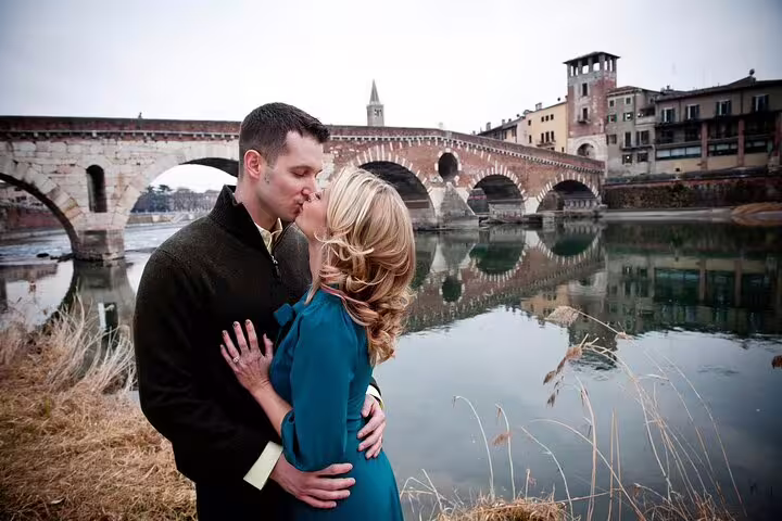 Romantic couple kissing by the historic Ponte Pietra in Verona, perfect for a professional photoshoot experience.