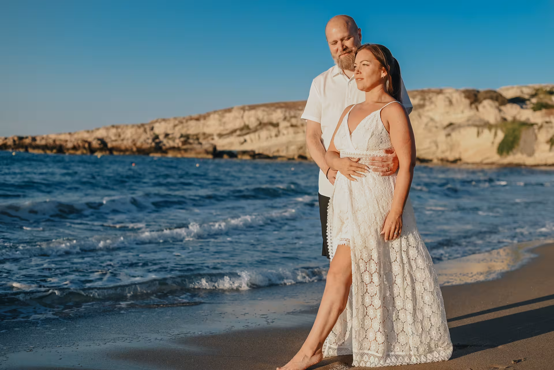 Romantic couple embracing on a sandy beach during a sunset photoshoot at the Port of Hersonissos.