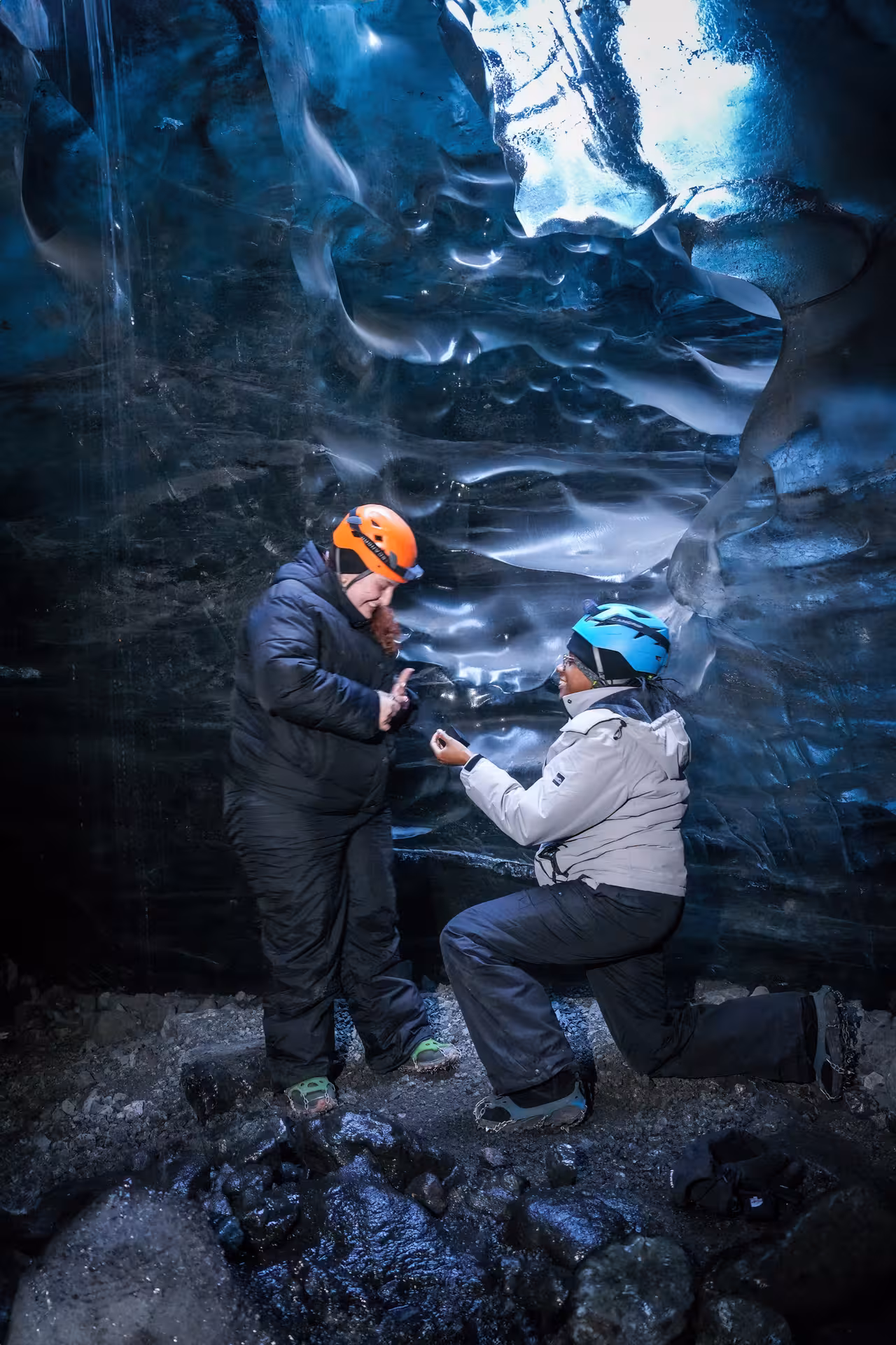 Romantic glacier cave proposal moment in Iceland with couple kneeling amid dramatic blue ice formations