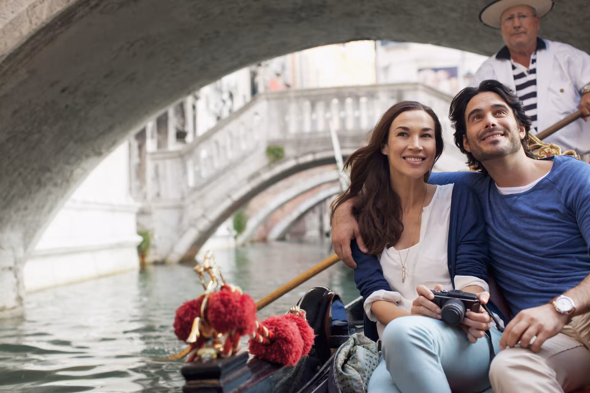 Happy couple enjoying a romantic gondola ride under a Venetian bridge during their St. Mark's Basin tour.