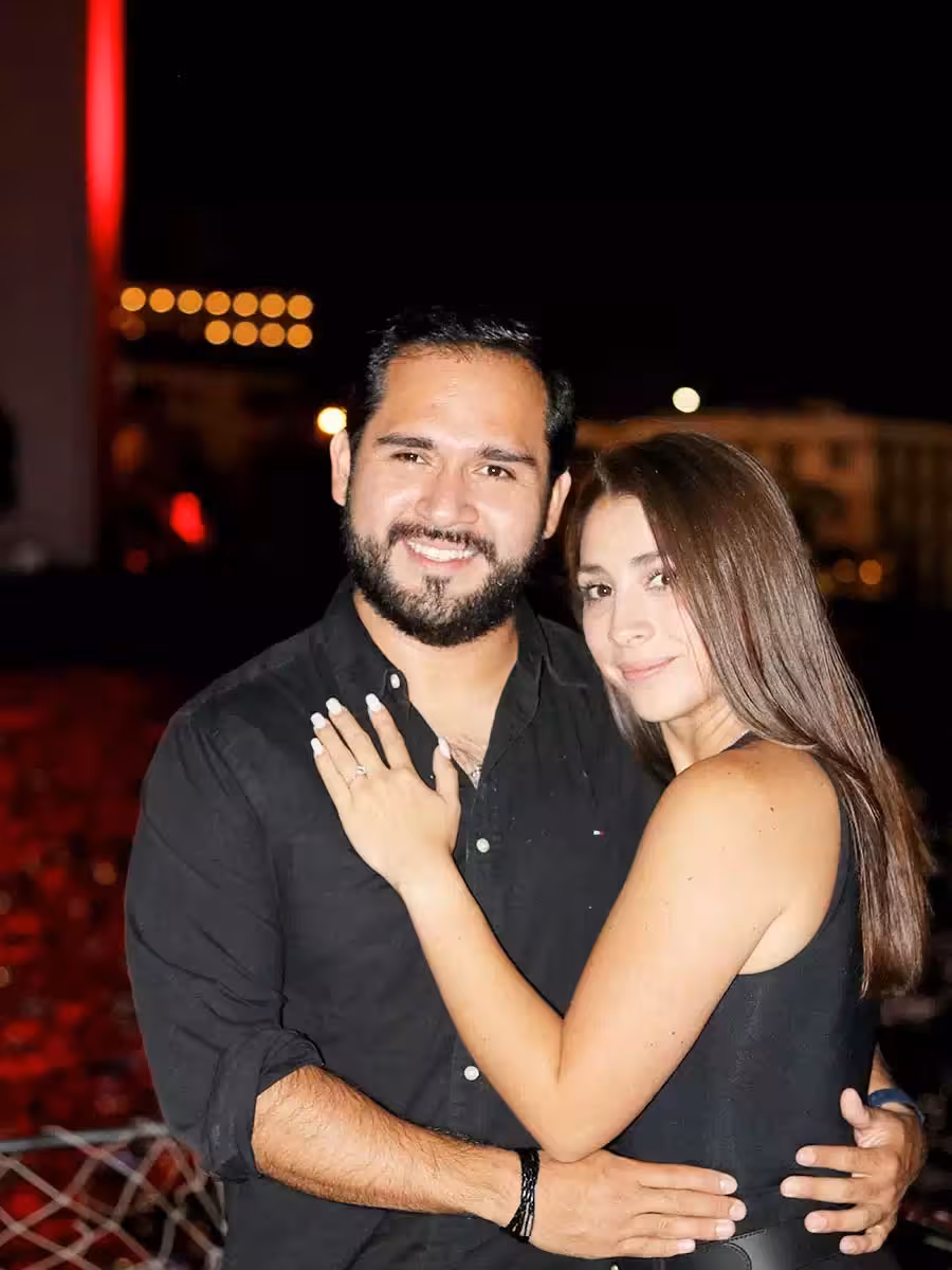 Couple hugging on a romantic marriage proposal night tour, engagement ring visible with city lights behind