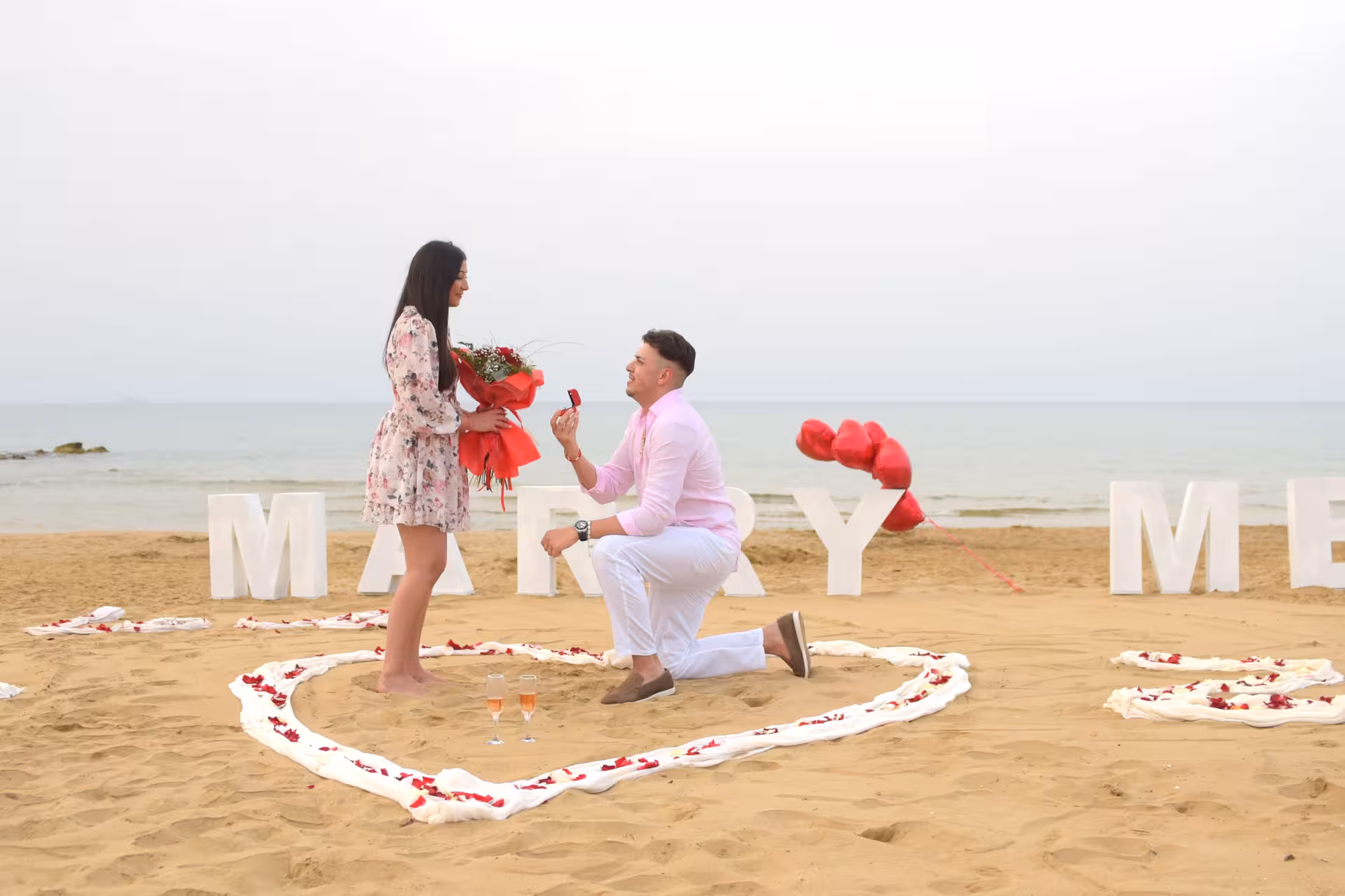 Romantic beach proposal at Heraklion Venetian Port with couple, heart-shaped decor, and backdrop of the serene sea.