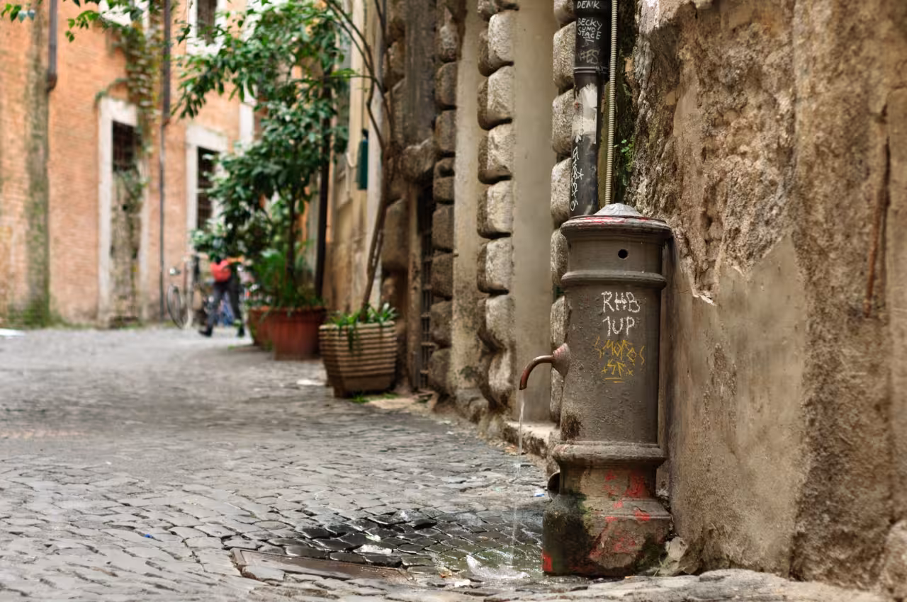 Cobblestone alley in Rome with historic stone wall and vintage fountain, perfect for a guided walking tour