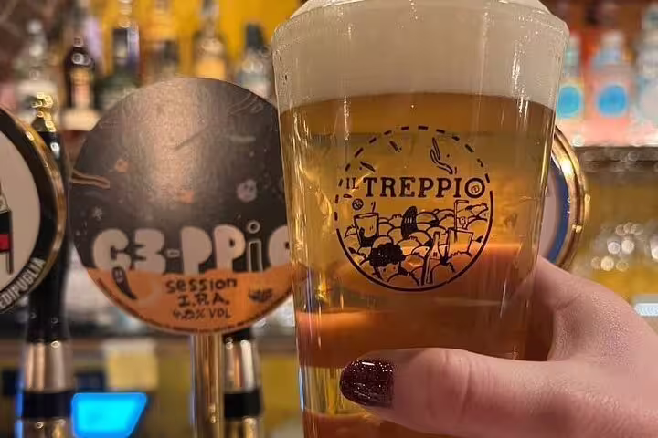 Hand holding a frothy glass of craft beer at a local bar in Rome, Italy, during the Vatican's Craft Beer Private Tour.