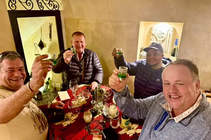 Group of friends toasting green liqueur shots during the Rome Fabullus wine pairing experience in a cozy enoteca