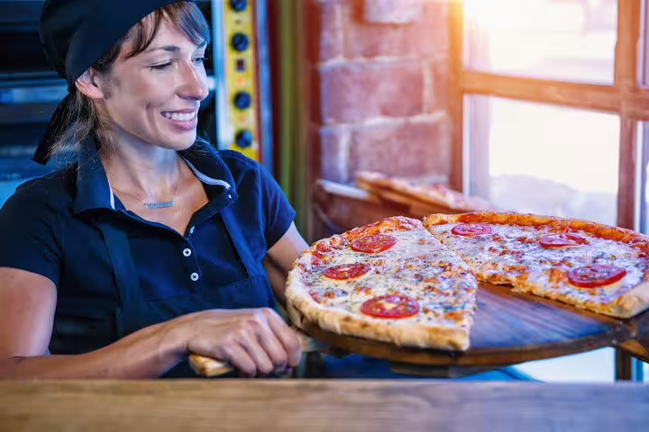 Smiling chef presents freshly baked pizza in a cozy Roman pizzeria, highlighting family fun on the Bella Roma private tour.