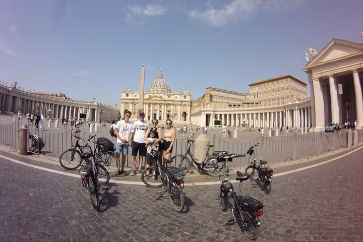 Tourists with e-bikes gather at St. Peter's Square on the Rome Highlights E-Bicycle tour, capturing iconic Vatican views.