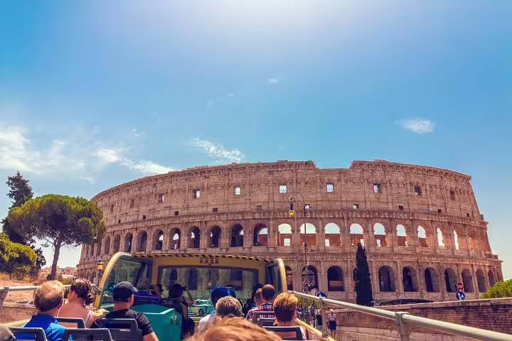 Tourists on an open-top hop on hop off bus passing the Colosseum on a sunny Rome sightseeing and Vatican fast track tour
