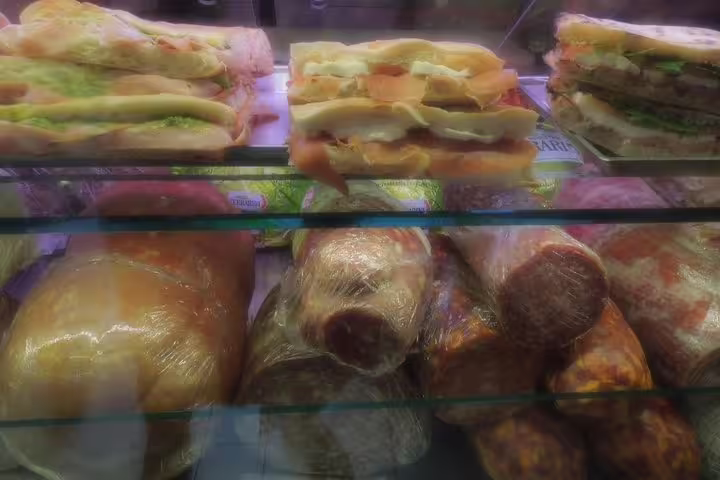 A glass display case filled with fresh Italian sandwiches and wrapped street food snacks in Rome Monti district
