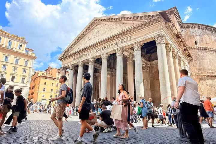 Tourists explore the iconic facade of Rome's Pantheon under a clear blue sky, highlighting its historical significance.