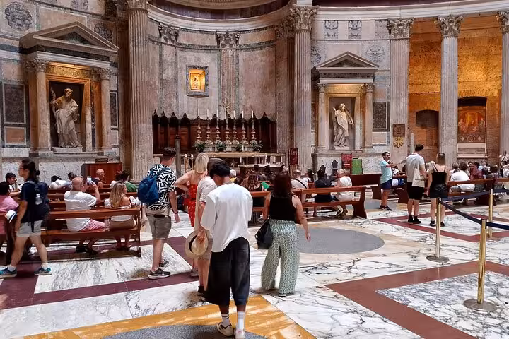 Visitors admire the historic interior of Rome's Pantheon, showcasing its grand columns and ancient statues, with a digital audio guide.