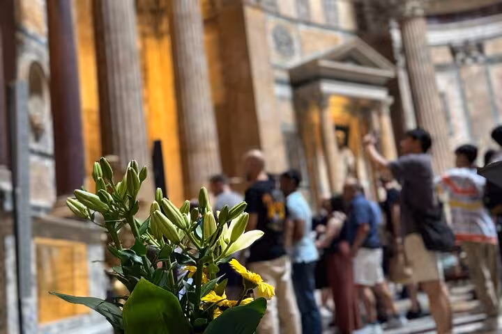 Tourists exploring the majestic interior of Rome's Pantheon with vibrant flowers in the foreground.