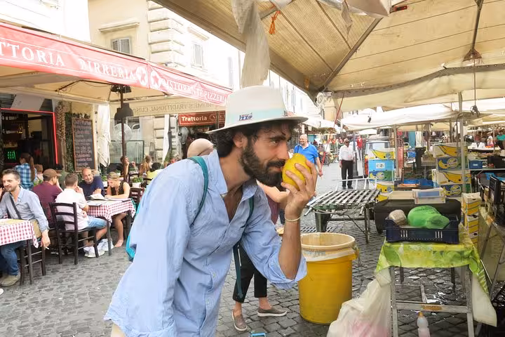 Man savoring the aroma of fresh produce at a local market in Rione Parione, Rome, during a private food tour.