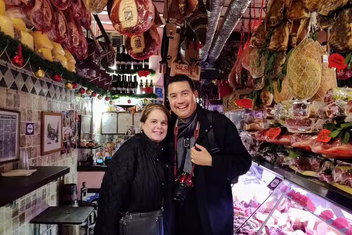 Tourists smiling inside a traditional Roman salumeria filled with cured meats on a Campo de Fiori food tour