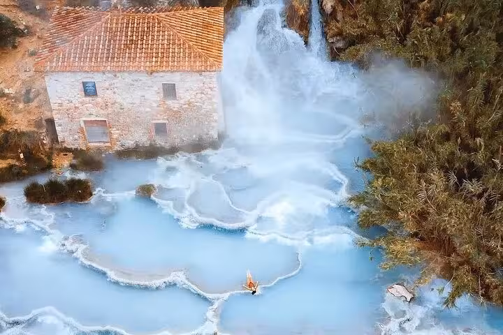 Aerial view of Terme di Saturnia's steaming thermal pools and historic building, perfect for a Rome to Saturnia transport tour.