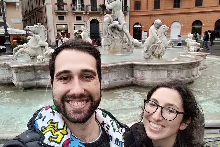 Couple smiling in selfie at ornate Roman fountain in Piazza Navona, Rome