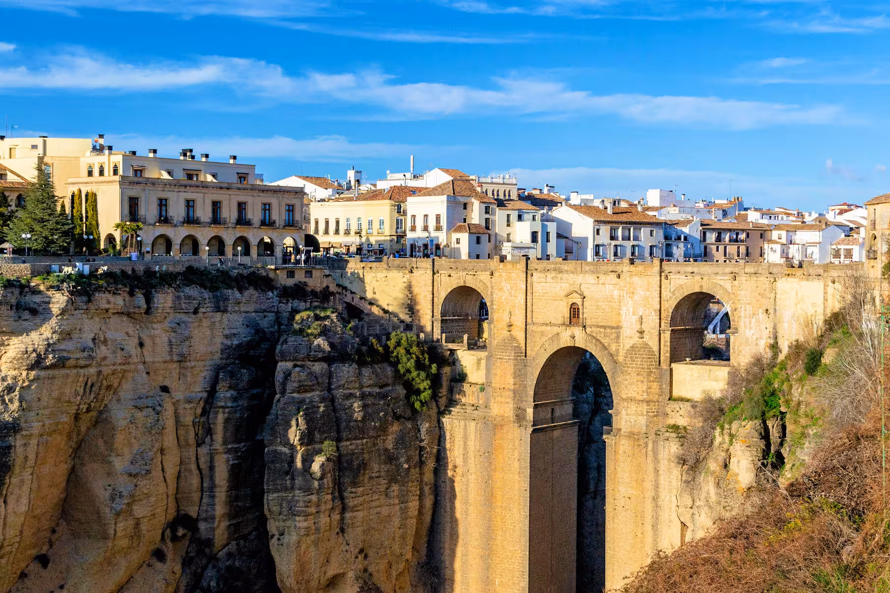 Scenic view of Ronda's iconic Puente Nuevo bridge spanning a dramatic gorge under a clear blue sky, perfect for day trips.