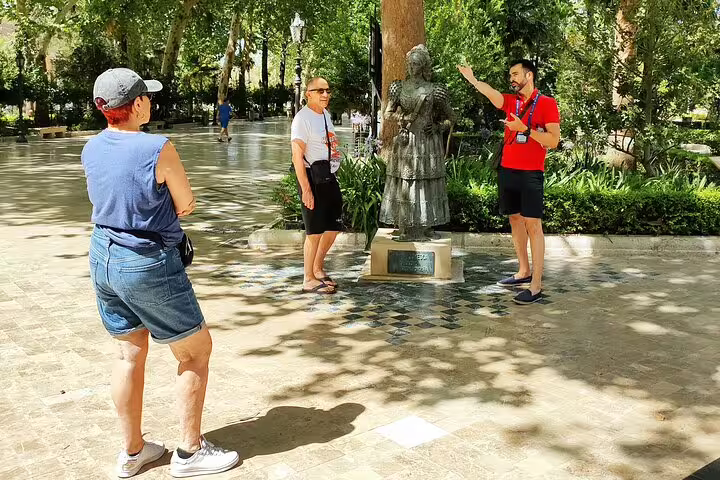 Tourists enjoy a guided tour around a statue in a lush park in Ronda, Spain, highlighting cultural insights.