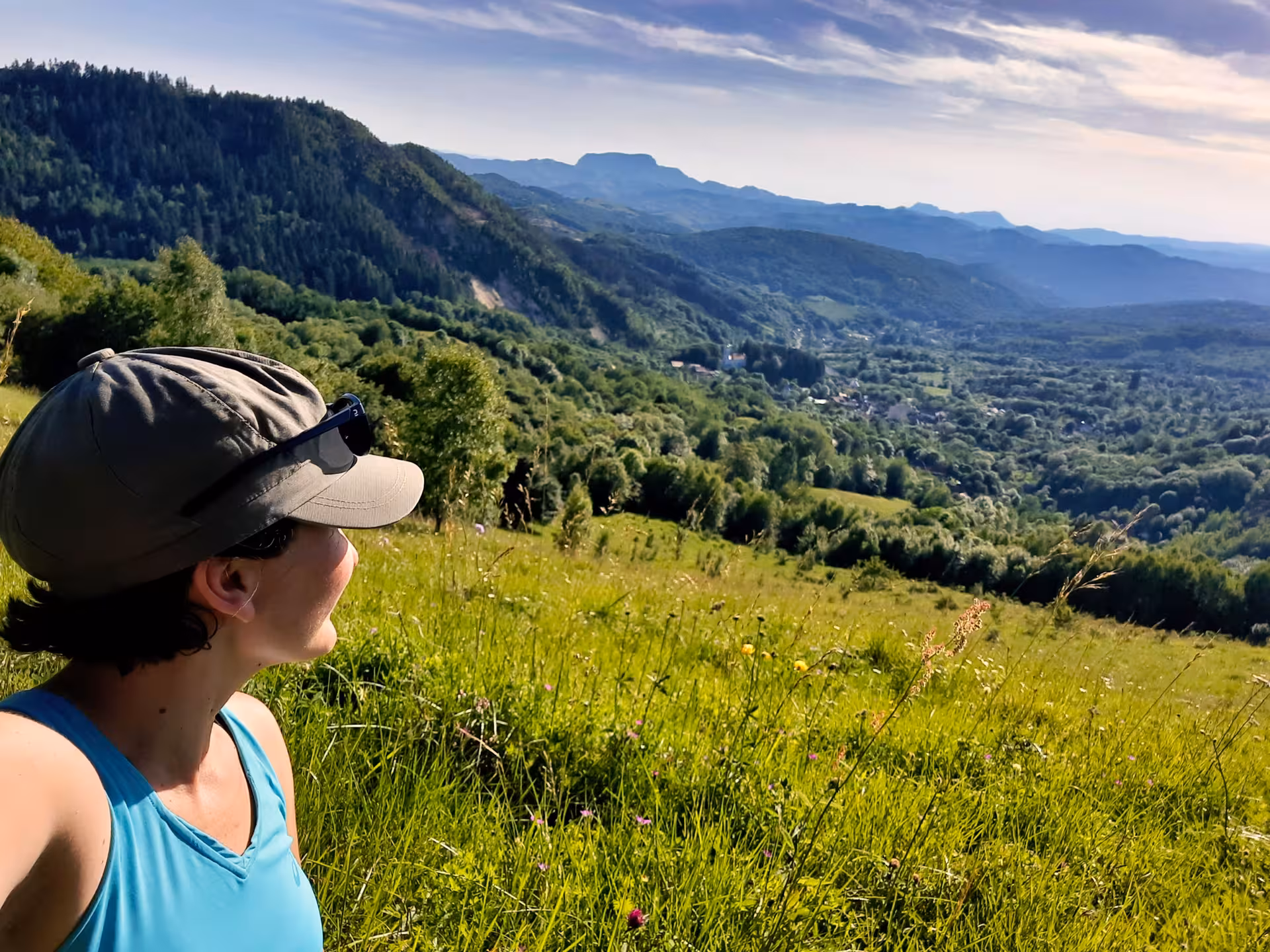 Hiker in cap gazing at lush green Apuseni Mountains valley with village below on sunny day