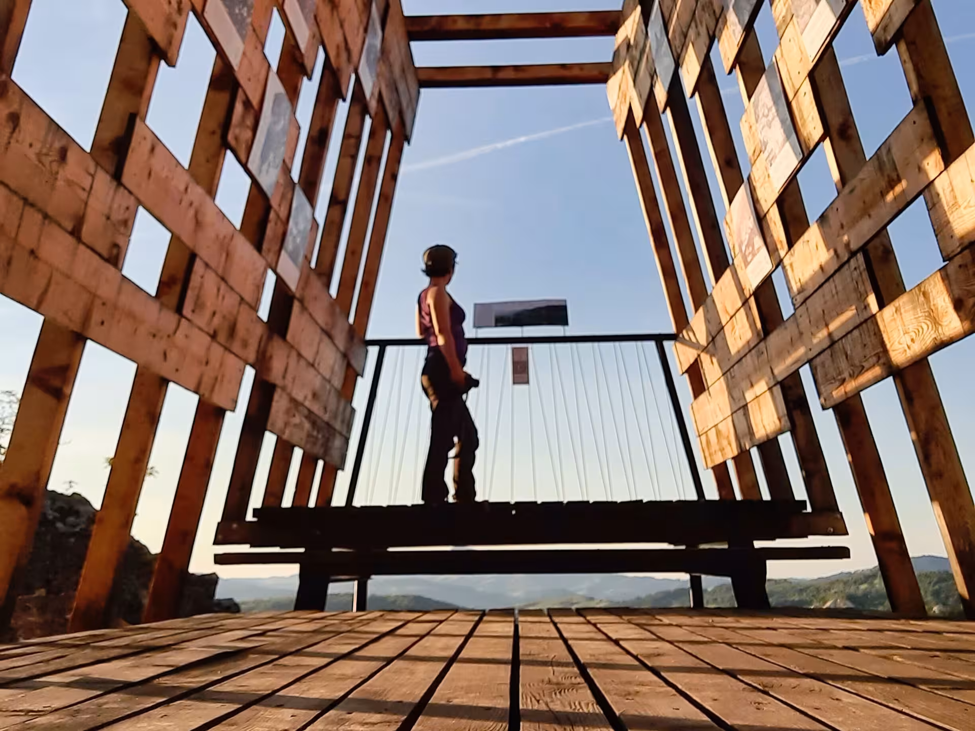 Hiker standing on wooden observation deck overlooking Apuseni Mountains landscape at golden hour