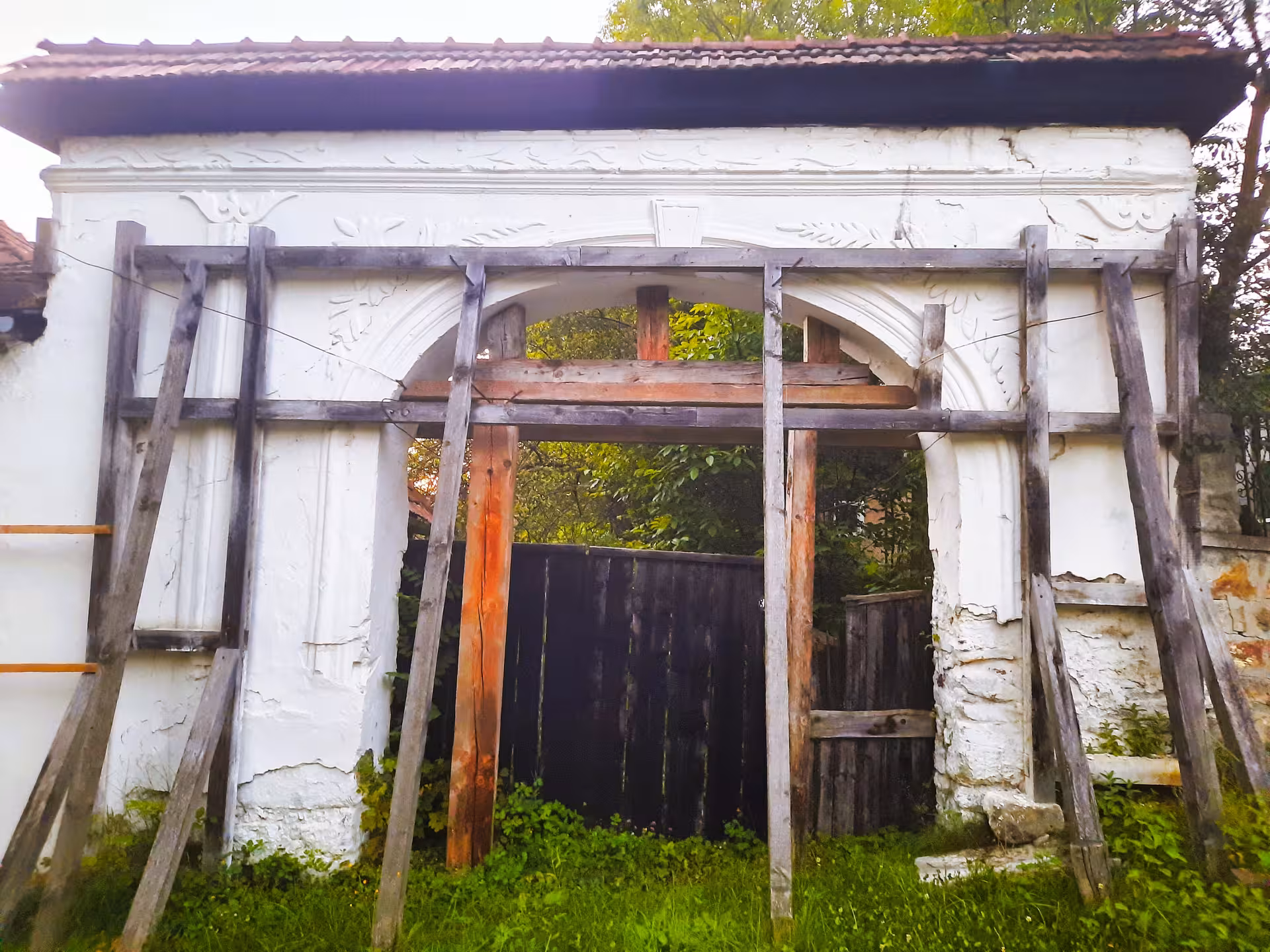 Ornate white arched gate with wooden scaffolding supports at historic Rosia Montana, Apuseni Mountains