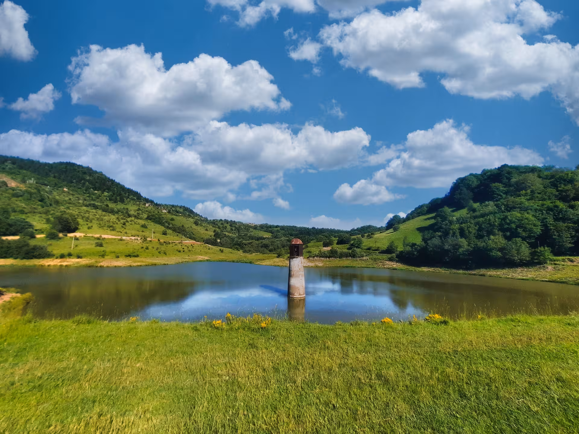 Calm reservoir with intake tower surrounded by green hills in Apuseni Mountains, Romania