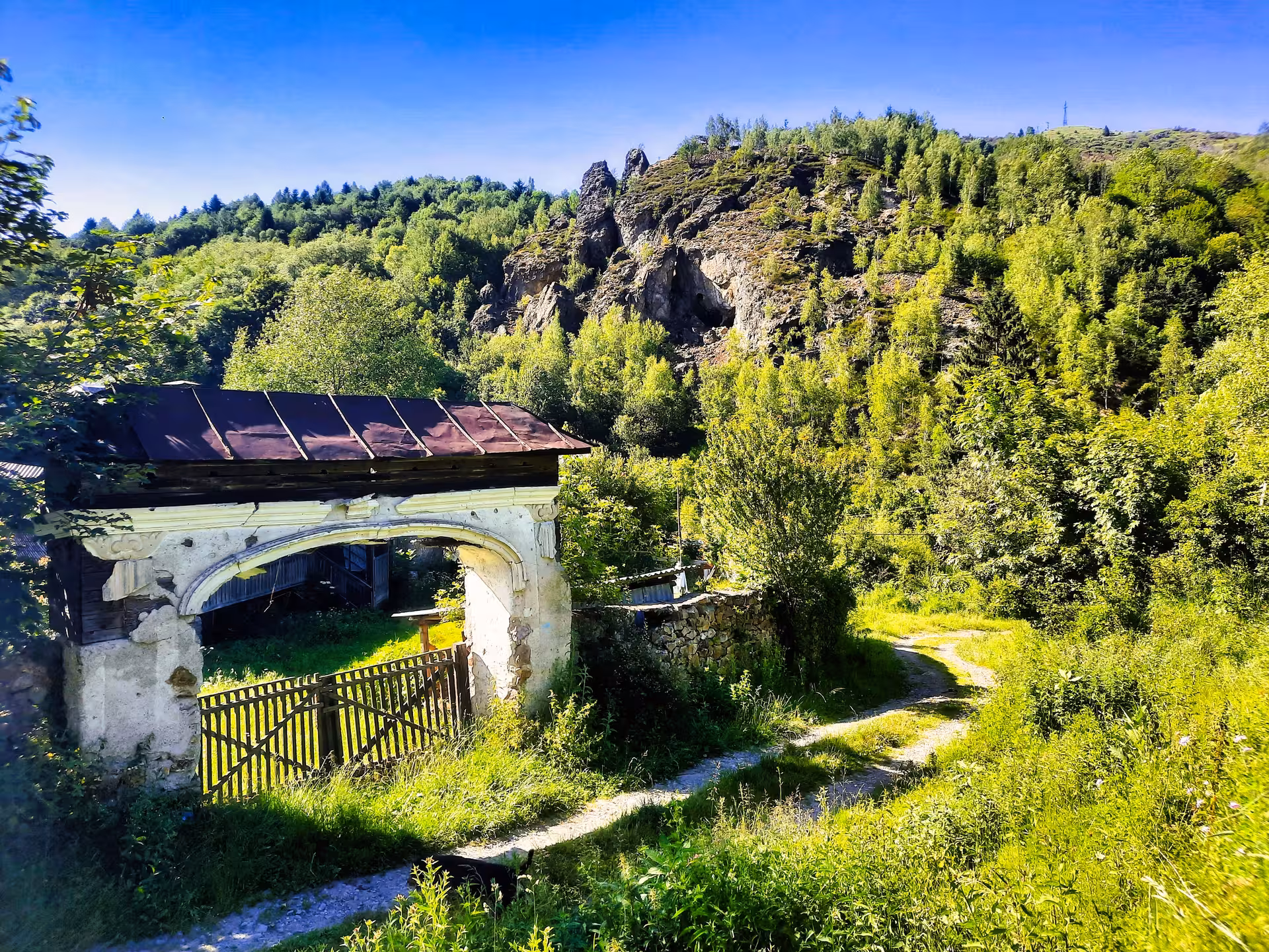 Ruins of an old stone arched gate surrounded by lush greenery with rocky cliffs in Rosia Montana, Apuseni Mountains