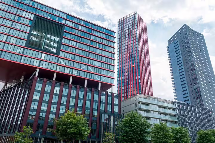 Modern red and glass skyscrapers in Rotterdam city center against a cloudy sky
