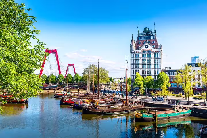 Historic boats moored at Rotterdam's Old Harbour with the iconic White House building and red Willemsbrug bridge in background