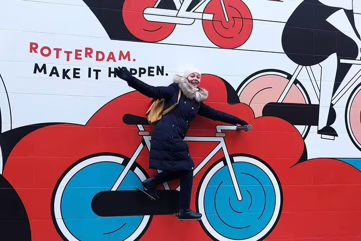 Traveler posing by Rotterdam street art mural with bicycles and “Make it happen” slogan on private walking tour