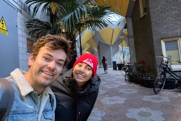 Two smiling tourists taking a selfie in front of Rotterdam's iconic yellow Cube Houses architecture