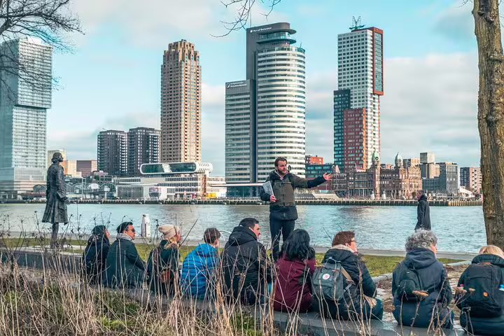 Group listens to local guide by Maas River with Rotterdam skyline, highlights and hidden gems walking tour