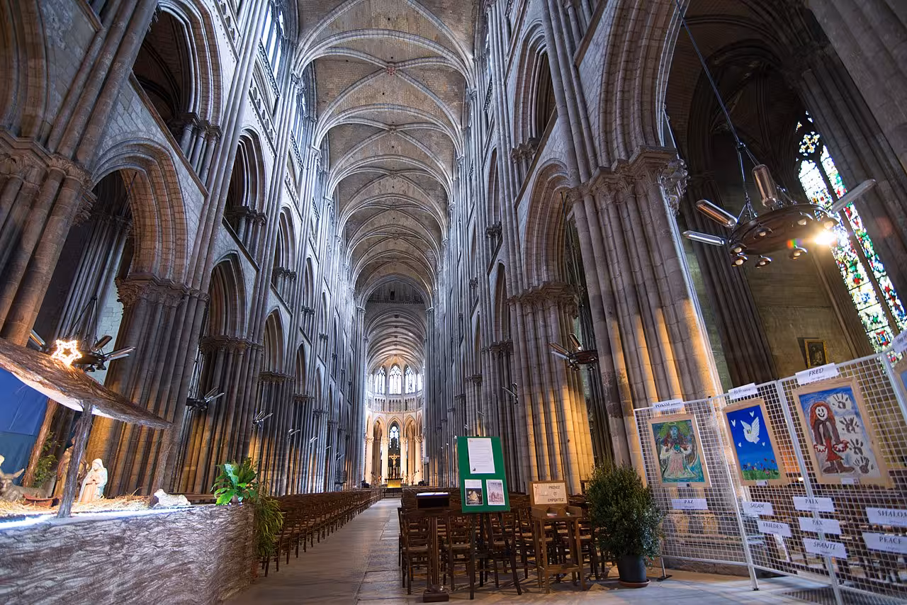 Gothic vaulted nave of Rouen Cathedral with soaring stone columns and colorful stained glass windows