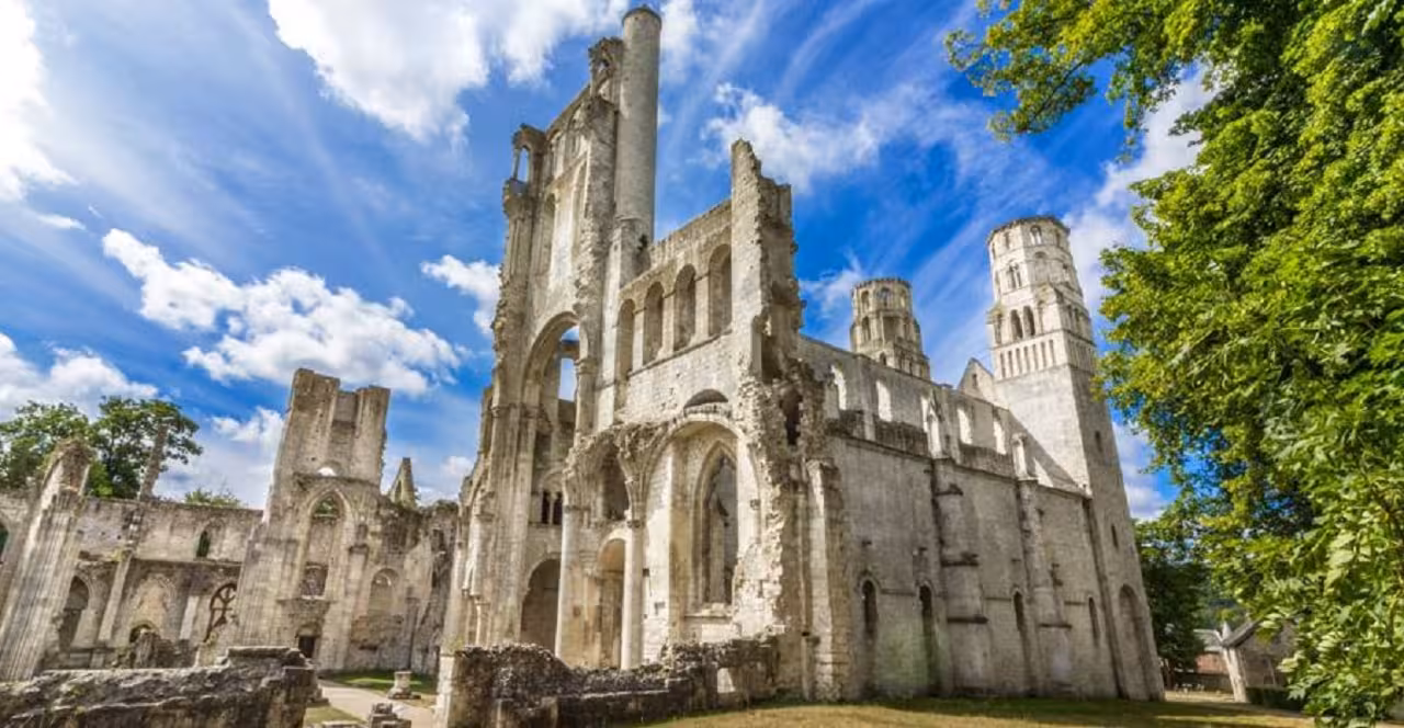 Gothic abbey ruins with tall stone towers and arched windows under blue sky in Normandy, France