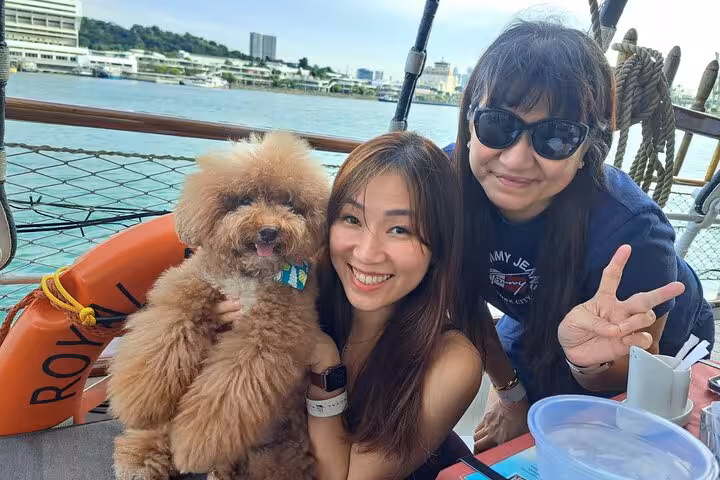 Smiling guests with a fluffy dog enjoying the Royal Albatross Dog Cruise against a scenic waterfront backdrop.