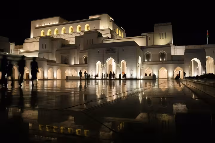 Illuminated Royal Opera House Muscat at night reflecting on wet marble plaza during evening heritage walking tour