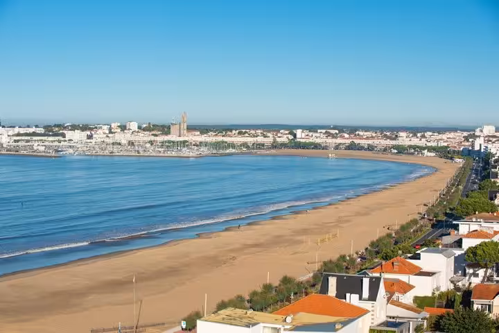 Aerial view of Royan's curved sandy beach and bay with city skyline on a clear sunny day
